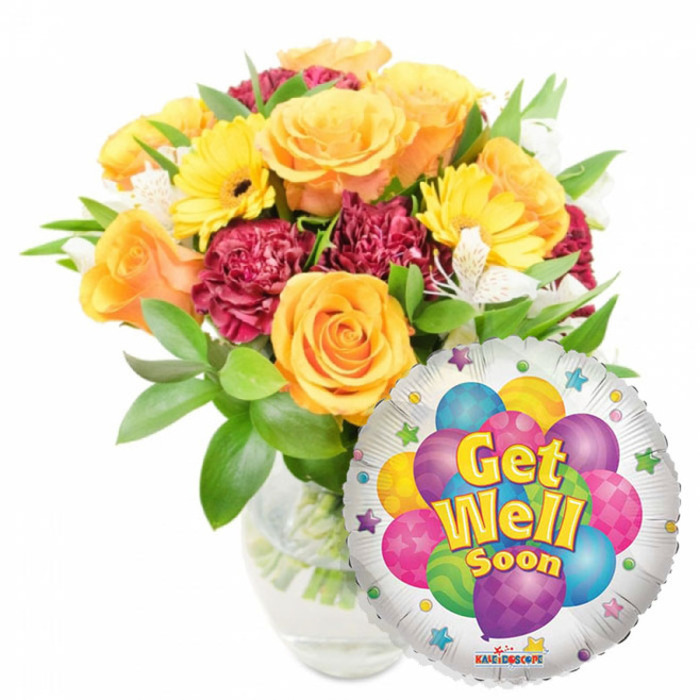 A carefully composed get-well bouquet photographed against pristine white, the display feels warm, hopeful and professionally arranged. The floral centerpiece occupies the left-to-centre plane: large, opening roses in amber-orange and deep golden yellow create a soft, spiralling focal point, their velvety petals catching a diffused light that enhances the blooms' warm tones. Interspersed are bright yellow gerbera daisies with clearly defined dark centres that contribute a sunny, graphic note, while densely ruffled carnations in maroon or deep magenta furnish textural contrast and a sense of depth. Slim sprays of white alstroemeria-tiny, freckled trumpets-peek through as luminous accents, their delicate petals adding air and refinement. Fresh green foliage in varied shapes wraps around the flowers, the glossy leaves providing a lively backdrop and supporting the bouquet's architecture. The stems are visible through a transparent glass vase, the clear water reflecting a soft glint. At the lower right, a metallic silver Mylar balloon partially overlaps the flowers, its surface catching highlights and showing a central motif of playful, cartoon-like balloons in bright blue, purple, pink, yellow and green, embellished with stripes, polka dots and subtle checker patterns. Prominently legible, cheerful lettering spells out Get Well Soon in yellow and blue, while small starbursts and a tiny KALEIDOSCOPE logo rest at the balloon's rim. The overall feel is compassionate and buoyant-perfect for sending to someone convalescing at home near Greenhithe Station or to cheer a patient recovering at a nearby clinic.
