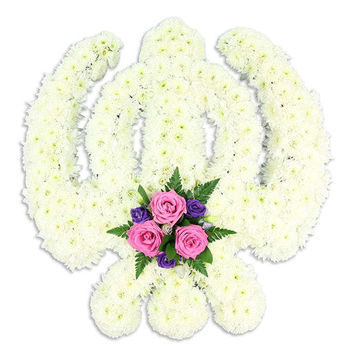 A solemn yet elegant Sikh Khanda floral tribute fills the frame, photographed against a bright white background that highlights the purity of the design. The Khanda symbol, central to Sikh faith, is clearly defined: the upright double-edged sword stands tall in the middle, surrounded by the unbroken circle of the chakkar, with two curved kirpans crossing at the base like protective wings. Every part of this emblem is built from densely packed white chrysanthemum heads or similar small blooms, meticulously arranged by hand. The tightly clustered petals create a soft, velvety surface that appears both plush and pristine, with subtle tonal variations from cool white to creamy ivory. The lighting is gentle and even, casting a delicate halo of shadow that gives the arrangement a three-dimensional feel, as though it rests on a table in a quiet room in Greenhithe, not far from the calm waters by the pier.
Nestled at the bottom centre of the floral Khanda is an accent posy that introduces colour and emotional focus. Three fresh pink roses, their petals slightly cupped and velvety to the eye, form the heart of this cluster. Their soft blush tones convey tenderness, love, and a sense of personal farewell. Around them, smaller deep purple blooms-likely lisianthus or freesias-are arranged to provide depth and a quietly regal note. Rich green fern fronds and foliage surround the flowers, softening transitions and adding natural movement. The composition of white, pink, and purple speaks of peace, devotion, and remembrance, making this tribute a fitting choice for Sikh funerals, memorials, or commemorative services in Greenhithe and nearby areas. Crafted with care by expert florists, the piece honours both religious symbolism and the intimate emotions of a family saying goodbye.