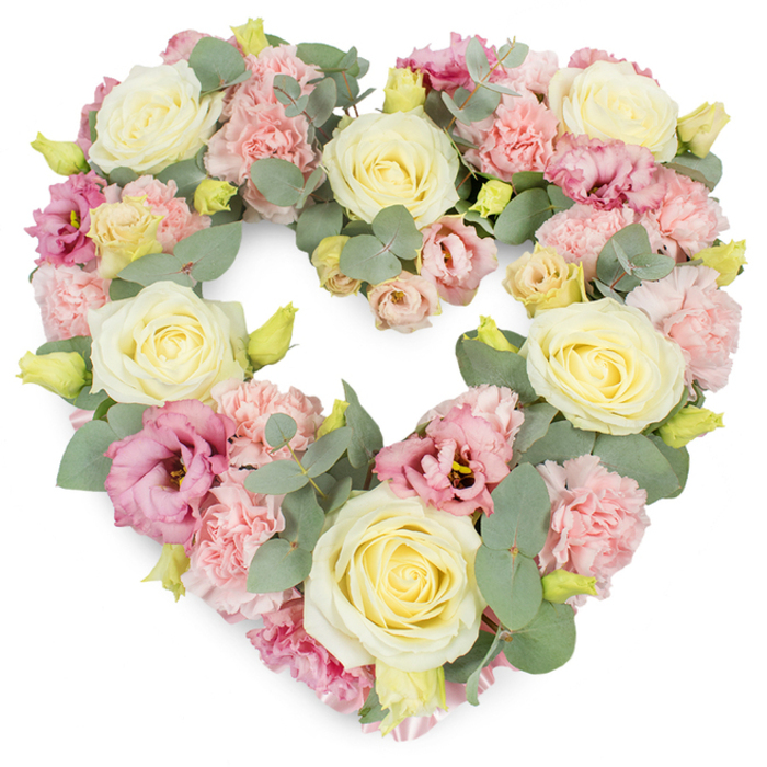 An elegant, heart-shaped condolence wreath is presented in full view, its outline perfectly drawn in blooms that span from soft cream to delicate pink, with just enough deeper colour to convey heartfelt emotion. The entire heart is lushly filled, giving it a generous, abundant appearance while remaining serene, much like the tranquil river paths around Greenhithe. At first glance, the eye is drawn to the creamy ivory and pale yellow roses scattered evenly across the surface; their petals are tightly layered in classical spirals, each one forming a rounded, velvety bloom that anchors the design with grace and quiet strength. Surrounding and embracing these roses are clusters of pastel pink carnations, whose frilled, almost feathery petals create a soft, tactile texture across the heart, inviting a sense of closeness and comfort. Deeper notes of colour come from the magenta and mauve-pink lisianthus blossoms, some fully open with gently rippled edges, others more cupped and modest. These blooms add depth and subtle drama, mirroring the complex emotions of grief, love, and remembrance. Interlaced throughout the generous florals are sprigs of eucalyptus, their rounded, silvery-green leaves following the curves of the heart and providing both structure and a cool, calming contrast to the warm petals. Here and there, tiny yellowish-green buds appear, a quiet but hopeful reminder of life's continuity. Against the white background, the arrangement feels almost suspended in stillness. A piece like this, lovingly arranged by Flower Delivery Greenhithe, would be chosen to accompany a funeral service, cremation, or memorial gathering, offering a gentle, dignified tribute from family, friends, or colleagues.