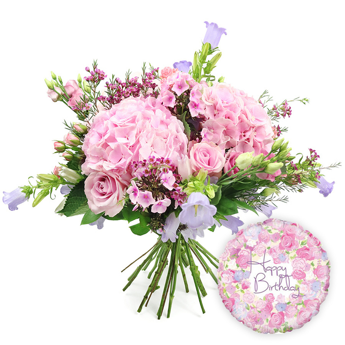 A beautifully composed birthday scene unfolds against a flawless white background, where a hand-tied bouquet and a foil balloon sit side by side, creating a sense of joyful occasion. The bouquet takes centre stage, crafted in a generous, rounded shape and dominated by large, blush pink hydrangea heads. These hydrangeas form lush, voluminous clusters, with countless tiny petals catching the light and imparting a rich, velvety softness to the arrangement. Weaving in and out of these plush pink mounds are soft pink roses, their classic shapes and layered petals adding structure and romantic charm. Some roses are fully open, displaying intricate spirals, while others remain tightly furled buds, suggesting longevity and the slow unfolding of blooms over several days in a Greenhithe living room. Between the larger blossoms, dainty clusters of fuchsia or magenta-toned waxflowers add a lively contrast and fine texture, preventing the palette from feeling too uniform. Punctuating the design, bell-shaped campanula flowers in gentle lavender and periwinkle blue extend upwards, providing vertical movement and a cool-toned counterpoint reminiscent of twilight skies above the nearby Thames. A mix of leafy greens wraps around and threads through the bouquet, from narrow, spear-like leaves to broader, more rounded foliage, enhancing the natural, garden-fresh impression you would expect from a skilled local florist. The stems at the bottom are tightly gathered and clearly visible, highlighting the hand-tied craftsmanship. To the lower right, a round, metallic foil Happy Birthday balloon completes the gift. Its surface is adorned with an intricate floral pattern of tiny roses and buds in shades of pink, lavender, and cream, while the central Happy Birthday message is written in elegant purple script. The image conveys a complete, ready-to-give birthday gift set, ideal for celebrations across Greenhithe, from riverside apartments to family homes near local parks.