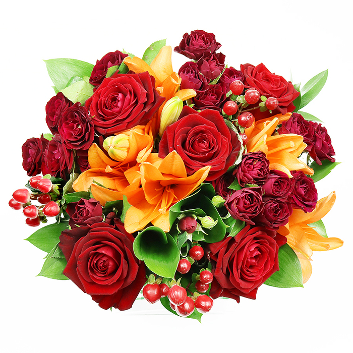 Viewed from a top-down angle on a pristine white backdrop, this dense, circular bouquet reads like a small celebration-warm, luxurious and meticulously arranged. At the center, several fully opened deep red roses display unfurling velvet petals that fold toward delicate inner cores, imparting an enduring sense of romance. Bright orange Asiatic lilies interrupt the red with trumpet-like confidence; some lilies bloom wide with visible stamens and dark speckling, while others are poised in elegant bud forms, suggesting movement and future blossoms. Interwoven among these primary blooms are tight clusters of dark burgundy spray roses, their compact heads creating a sumptuous, velvety texture and deeper tonal layers. Polished red hypericum berries appear in small groups, gleaming like tiny cherries and adding playful punctuation and tactile variety to the arrangement. Generous green foliage-broad, glossy salal or ruscus leaves-emerges between flowers, providing cooling contrast and shaping the bouquet's silhouette. The soft, even lighting highlights petal surface and berry gloss without dramatic shadows, and the imagined scent is a gentle blend of rose warmth with the slightly sweet-spicy note of lilies. This bouquet is ideal for gifting on anniversaries, marking celebrations, or lending seasonal warmth to home décor. As a local florist in Greenhithe, Flower Delivery Greenhithe would describe this design as a piece that feels at home beside a window overlooking the Thames or on a console near Bluewater's lights-comforting, elegant, and unmistakably heartfelt.