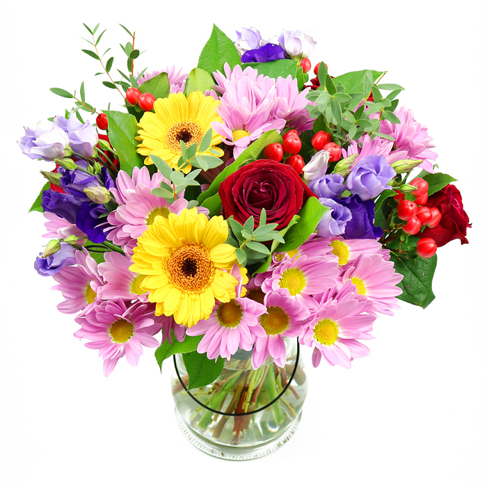 The image presents a vibrant mixed-flower arrangement displayed in a transparent glass vase, positioned against a white background so that the colours and shapes are remarkably crisp. At the core, dusky red roses unfurl in velvety layers, lending the arrangement a romantic, almost classic feel, like a quiet evening view across the Thames from Greenhithe's riverfront. Standing alongside them, two sunshine-yellow gerbera daisies with dark, warm-toned centres introduce a more playful note, their flat, round blooms echoing the shape of cheerful sunbursts. Encircling this central cluster is a generous ring of pink chrysanthemums and daisy-style flowers, their many slim petals fanning out around small yellow centres, creating soft cushions of colour and a sense of gentle fullness. Woven between these blooms, slender stems of purple and lavender lisianthus rise gracefully, some tipped with tight buds, others opening into softly ruffled, bell-shaped flowers, adding cool, sophisticated accents that contrast beautifully with the warmer tones. Among the petals, you can spot bright red hypericum berries, gathered in small clusters on thin stems; their smooth, bead-like surfaces provide a sleek, contemporary texture. A lush collar of greenery frames the bouquet, combining deeper green, broader leaves with more delicate, lighter sprigs, reminiscent of the plant life that lines walking routes around Greenhithe and Ingress Park. Through the glass vase, the stems are clearly visible, carefully trimmed and neatly splayed in clear water, revealing the structured base that supports the blooming dome above. The overall impression is of abundant joy and heartfelt generosity, making this bouquet ideal for birthdays, housewarmings, or a congratulatory delivery to homes and offices around Greenhithe, where a burst of colour and fragrance can instantly transform a room.