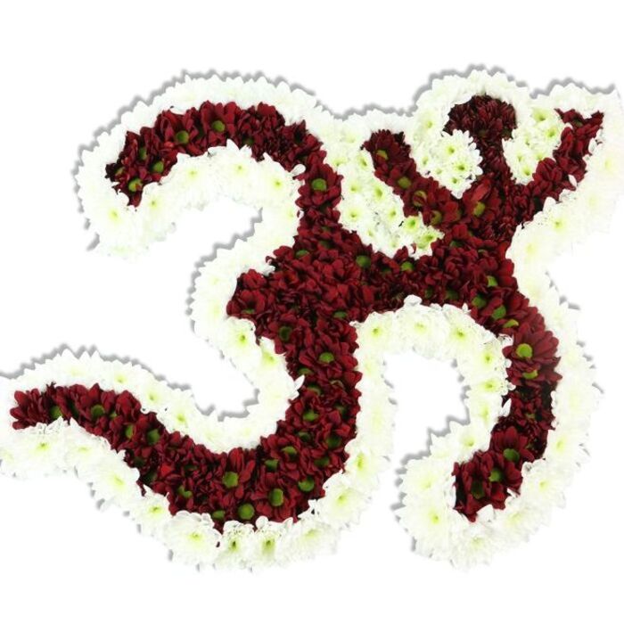 This sculptural floral tribute presents the sacred Om (Aum) symbol with exacting care, set against a stark white field that allows every petal to stand out. The central '3'-like form, the flowing downward stroke and the small crescent-and-dot element above are filled with rich maroon to deep red chrysanthemum-style blooms; many of those tiny flowers show bright lime-green centers that introduce subtle liveliness within the dark mass. Framing and contouring the whole symbol is a broad, undulating border of immaculate white spray chrysanthemums, their delicate petals softening the design and making the silhouette read with crystalline clarity. A soft drop shadow beneath conveys three-dimensionality, while studio lighting highlights the layered texture - petals overlapping like scales yet appearing soft and cool to the touch, with a muted, natural scent that suggests fresh-cut garden flowers.From my experience serving the Greenhithe community and nearby Bluewater venues, this piece fits moments of remembrance, spiritual ceremonies, or cultural celebrations that ask for a respectful, handcrafted floral emblem. Delivered carefully for display on an altar or memorial plinth, it communicates devotion through colour and form. At Flower Delivery Greenhithe we would source each bloom for freshness and place them densely to ensure durability and a plush, unified surface. The result is an image of tranquil intensity - a floral Om that reads as both symbol and offering, rooted in expert hands and local knowledge of ceremonial presentation near the Thames.