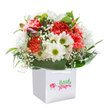 Joy springs vividly from this stunning arrangement, secured in a contemporary white gift bag, crafted with care for Greenhithe's community. The bouquet features a harmonious blend of soft coral and peach carnations-each frilled petal exuding gentle affection-interlaced with striking red carnations that bring vibrancy and depth. White daisies with bright, green-tinged centers lift the mood, their innocence reminiscent of blooms found along the River Thames. Airy sprigs of baby's breath swirl between these main flowers, their tiny blossoms adding lightness and charm. On the left side, a few shy purple-tinged buds nestle amid glossy, deep green leaves, conjuring the tranquil promise of wildflowers in early spring around Waterstone Park. Encircling the base, abundant broad leaves provide a natural couture that elevates the sense of structure and density within the piece. The bouquet's expertly shaped, full appearance bespeaks attentive, local craftsmanship-each element selected and placed for maximum freshness and joy. Strong white ribbon handles adorn the bag, ready to deliver happiness to a Greenhithe doorstep, whether for a birthday, milestone, or a spontaneous token of appreciation. This bouquet, a true expression of Greenhithe's floral artistry, radiates sincerity and is poised to bring uplifting beauty to any special occasion.